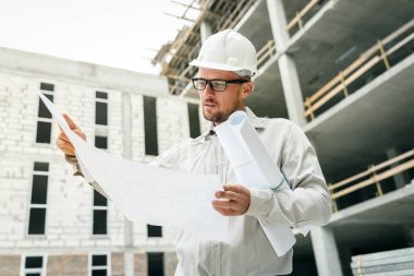 İnşaat mühendisi olarak teftiş planları inşaat alanı üzerinde beyaz bir kask. Geliştirme ve İnşaat Sanayi kavramı