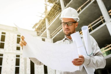 İnşaat mühendisi olarak teftiş planları inşaat alanı üzerinde beyaz bir kask. Geliştirme ve İnşaat Sanayi kavramı