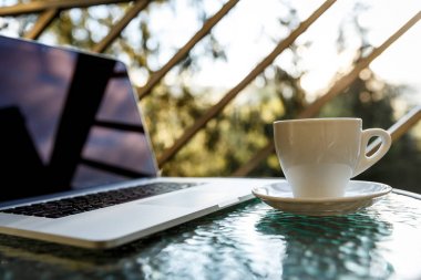 Beyaz çay ya da kahve fincanı ve balkon sehpasında dizüstü bilgisayar.
