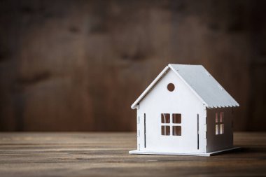 Kahverengi ahşap arka planda üçgen çatılı bir evin beyaz modeli. Gayrimenkul kavramı