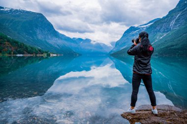 Nature photographer tourist with camera shoots Beautiful Nature Norway natural landscape. lovatnet lake. clipart