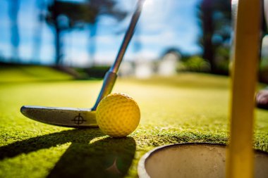 Gün batımında deliğin yanında sopayla birlikte mini golf topu.