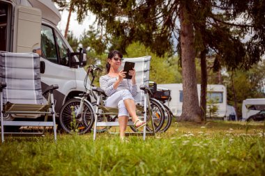 Kamp yakınlarında tablet bakarak bir kadın. Karavan araba tatil. Aile tatil seyahat, tatil gezisi kamyonet ve karavan RV Wi-fi bağlantı bilgi iletişim teknolojisi.