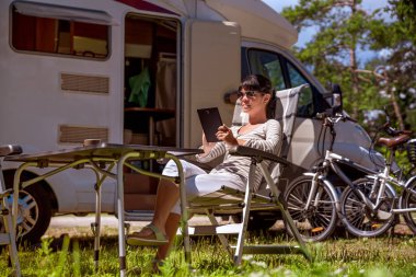 Kamp yakınlarında tablet bakarak bir kadın. Karavan araba tatil. Aile tatil seyahat, tatil gezisi kamyonet ve karavan RV Wi-fi bağlantı bilgi iletişim teknolojisi.
