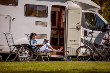 Kampın yanındaki dizüstü bilgisayara bakan kadın. Karavan tatili. Aile seyahati, karavanla tatil gezisi. Wi-fi bağlantı iletişim teknolojisi.