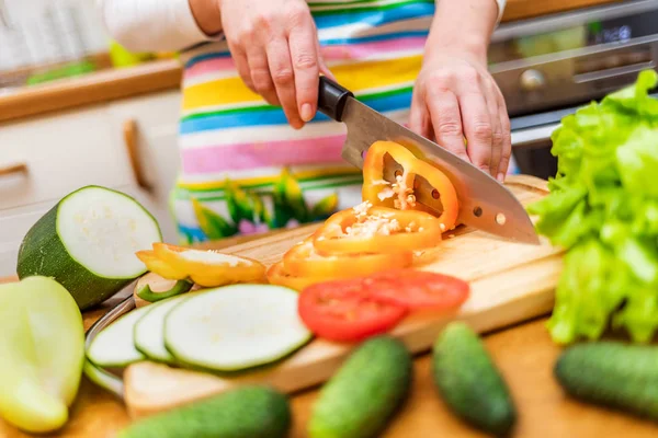 Female hands of housewife with a knife cut fresh bell pepper on chopping Board kitchen table