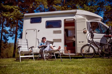 Kampın yanındaki dizüstü bilgisayara bakan kadın. Karavan tatili. Aile seyahati, karavanla tatil gezisi. Wi-fi bağlantı iletişim teknolojisi.