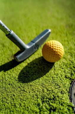 Gün batımında deliğin yanında sopayla birlikte mini golf topu.