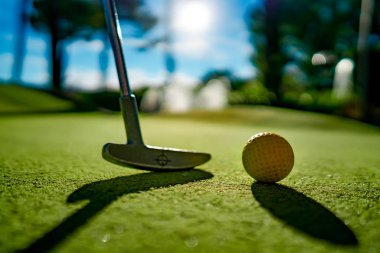 Gün batımında deliğin yanında sopayla birlikte mini golf topu.