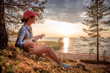 Gün batımında ukulele çalan kadın.