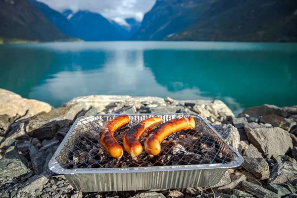 Grilling sausages on disposable barbecue grid. — Stock Photo, Image