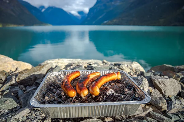 Salchichas a la parrilla en rejilla de barbacoa desechable. — Foto de Stock