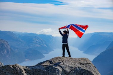 Doğanın arka planında Norveç bayrağı sallayan bir kadın.
