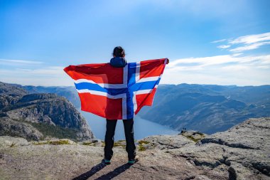Doğanın arka planında Norveç bayrağı sallayan bir kadın.