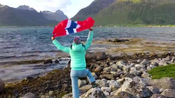 Жінка з розмахуючим прапором Норвегії на задньому плані природи — стокове відео
