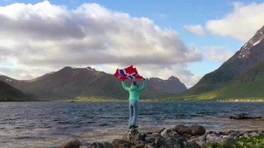 Doğanın arka planında Norveç bayrağı sallayan bir kadın.