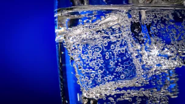 Vaso de agua con hielo sobre fondo azul oscuro — Vídeo de stock