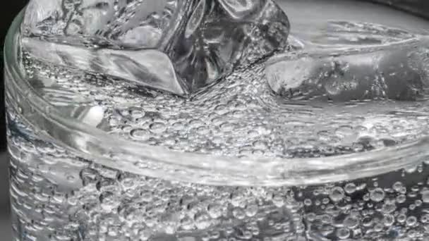 Glas Wasser mit Eis auf dunkelblauem Hintergrund — Stockvideo