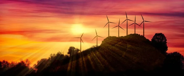 七座现代化风电场的横向构图在远处的山上 背景是晚霞的美丽落日 图库图片