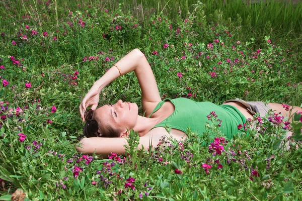 Güzel genç kız yeşil çimlerde yatıyor. — Stok fotoğraf
