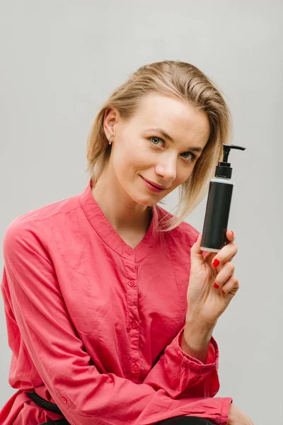 portrait of a female with cosmetics bottle black in hands, studio photo