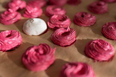 Pasta kağıdına yerleştirilmiş kıvrımlı desenli pembe kurabiyeler. Tatlı ve pişirme kavramları için mükemmel. Zarif gül renginde şekerleme sergilenen el yapımı mutfak sanatları..