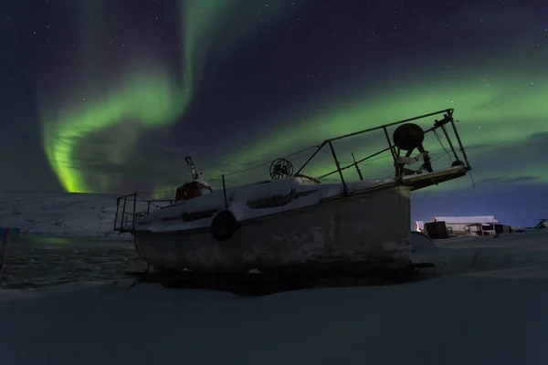 Old fishing boat on a background of aurora in winter