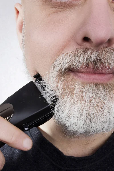 头发灰白的男人用电动剃须刀刮胡子 — 图库照片