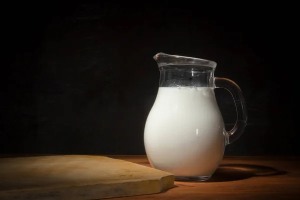 木桌上的玻璃水壶和新鲜牛奶 — 图库照片