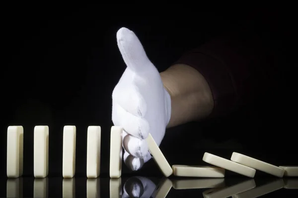 Een handje in een handschoen stopt de dominostenen die vallen — Stockfoto