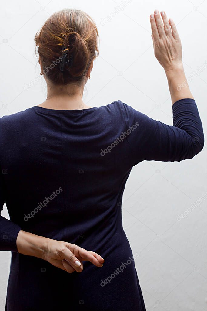 Woman takes an oath and holds her crossed fingers behind her back.