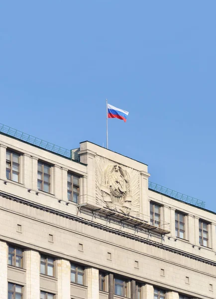 Russian national flag and coat of arms on top of the State Duma of the Russian Federation (Russian Parliament), Moscow, Russia.