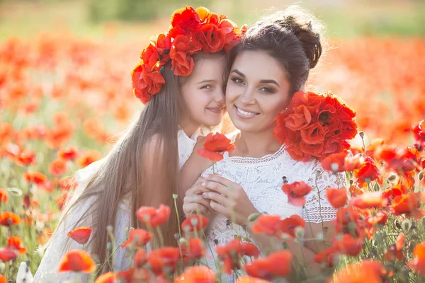 母とケシのフィールドに娘 美しい母と春の花畑で遊ぶ娘 新鮮な花日当たりの良い夏の日に彼女の母親と一緒にケシ畑の上を歩いての赤い花輪の少女 — ストック写真