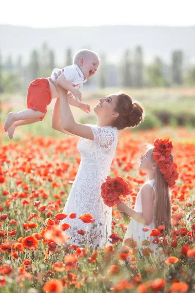 息子と娘が赤いケシのフィールド 小さな息子と春の花畑で娘と母 新鮮な花日当たりの良い夏の日にママと兄と一緒にケシ畑の上を歩いての赤い花輪の少女 — ストック写真