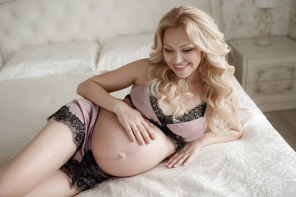 幸せな笑みを浮かべて妊婦ソファーに座っていると 彼女の腹を Caressing します ママ期待して赤ちゃん 妊婦腹 美しい妊娠中の女性 出産の概念 美しい妊婦ランジェリーを自宅で — ストック写真