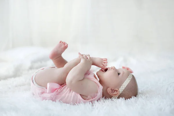 可爱可爱的女婴独自躺在白色的床上 小孩看着镜头 婴儿学习抓取白色背景 幸福女儿的肖像 婴儿时尚服装 一个5个月大的孩子一个人在玩 躺在雪白的床上 — 图库照片