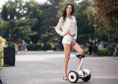 Güzel kadın güneş gözlüğü, beyaz bir bluz ve şort zaman şehir parkı açık havada yaz aylarında bir segway sürme harcıyor. Yeşil Park Elektrik mini vurgulu kurulu scooter ile genç esmer kız. İyi bir hava trendy ulaşım teknolojisinin