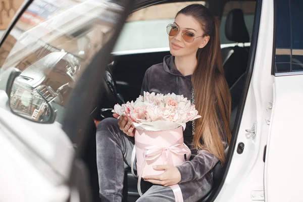 Girl with a large bouquet of white tulips in the car. Happy woman on valentines day. Young beautiful woman, sitting on the driver's seat in a car with a pink box full of tender, white, with a pink edging of beautiful flowers. Day of Love.