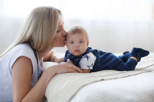 若い母親が彼女の生まれたばかりの子供を保持します 女性と生まれたばかりの少年は 白い寝室でリラックスします 若い母親は 優しく彼女の腕に彼女の生まれたばかりの息子を保持しています 自宅で家族 若い母親はいったん彼女の生まれたばかりの息子を再生 — ストック写真