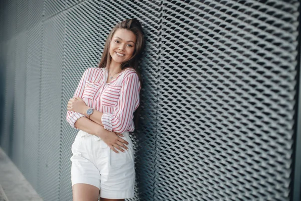 Fashion portrait of a sensual woman. External photo of an attractive brunette model in a white skirt and a striped blouse. Gorgeous portrait of a beautiful sexy woman outdoors in the summer on the city street. Natural beauty and lifestyle concept