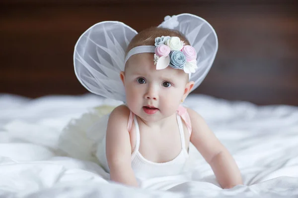 彼の後ろに天使の翼を持つ青い目の赤ちゃん 天使の翼を持つ赤ちゃん新生児 ブルースカイクラウドに座っている子供 女の子5 7ヶ月寝室の白いベッドに座って かわいい新生児の天使 — ストック写真
