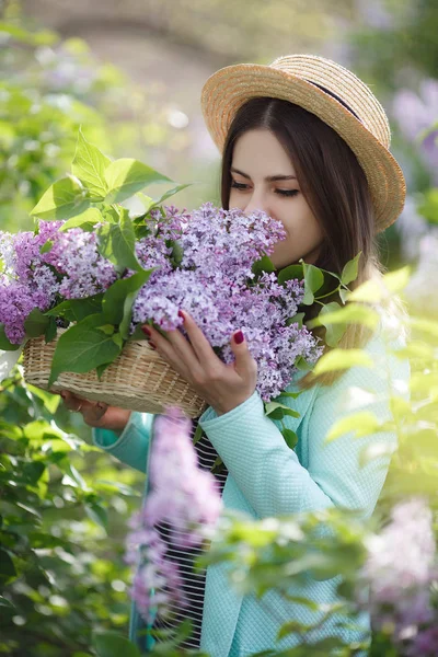 在一个阳光灿烂的日子里 年轻美丽的女人正享受着盛开的紫丁香的芬芳 美丽的女孩 一头乌黑的长发 戴着草帽 在春天的公园里享受着百合花盛开的芬芳 — 图库照片