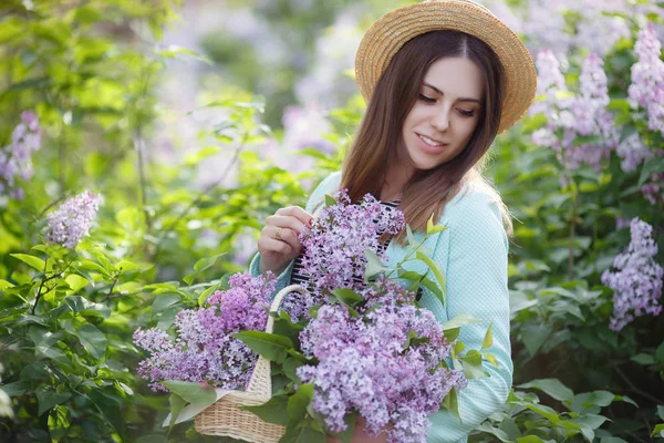 在一个阳光灿烂的日子里 年轻美丽的女人正享受着盛开的紫丁香的芬芳 美丽的女孩 一头乌黑的长发 戴着草帽 在春天的公园里享受着百合花盛开的芬芳 — 图库照片