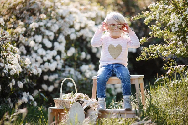 一个可爱的小女孩戴着一顶大草帽 独自在春天的公园里独自呆在户外 坐在白色开花的灌木丛背景上 春天的画像 一个迷人的小女孩走在花的公园里 — 图库照片