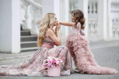 Güzel ince kadın ve küçük kızı, çiçekli şeftali ile bir saray sokakta, pembe renk güzel top Gowns giymiş, baharda açık havada eğlenmek. Sokakta güzel Abiye anne ve kızı