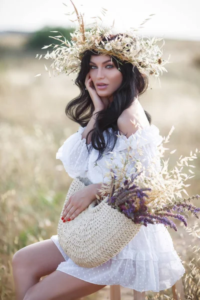 一个美丽的年轻女子 黑发长发 独自在日落时分在一片绿草丛中 女孩与一个美丽的花圈在干草和花在日落时在田野上摆姿势 — 图库照片