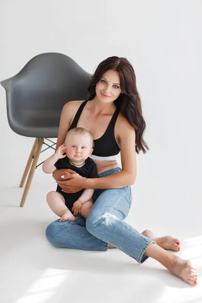 Jovem Mãe Macacão Jeans Segura Uma Criança Nos Braços Fundo — Fotografia de Stock