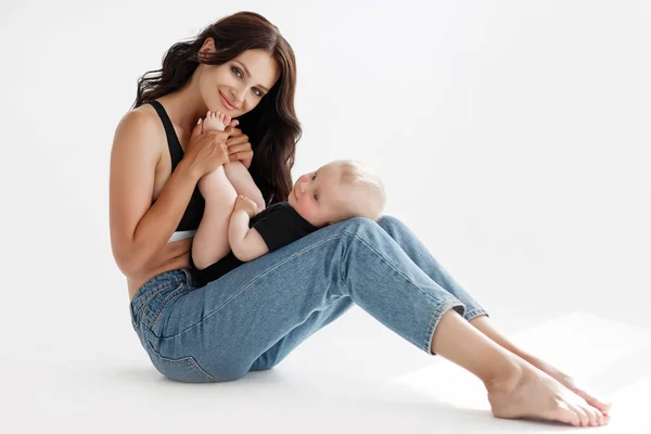 Młoda Kobieta Matka Kombinezonach Jeansowych Trzyma Dziecko Ramionach Białe Tło — Zdjęcie stockowe