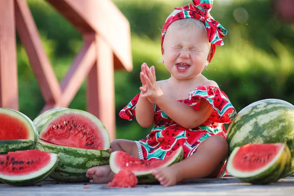 Child eating watermelon in the garden. Kids eat fruit outdoors. Healthy snack for children. Little girl playing in the garden holding a slice of water melon. Kid is smiling, enjoying eating fruit.Kid on a background of ripe red watermelons outdoors