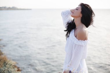 Sahildeki mutlu kadın. Deniz arka plan üzerinde yakın çekim güzel bir kız portresi. Sahilde bahar portresi. Genç güzel kız. Genç gülümseyen kadın açık havada portre. Okyanusun kayalık kıyısında güzel genç kadın